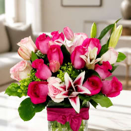 Pink roses and lilies arranged in a glass vase with a magenta ribbon