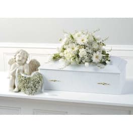 White floral arrangement on a white casket with an angel figurine beside it