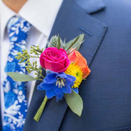 Colorful boutonniere with roses and a blue flower on a suit lapel