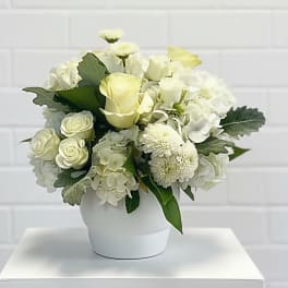 White floral arrangement in a white vase with roses and hydrangeas