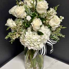 White roses and hydrangeas in a glass vase with a striped ribbon