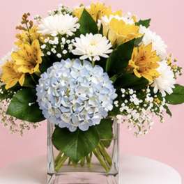 Bouquet of yellow and white flowers with a blue hydrangea in a clear glass vase