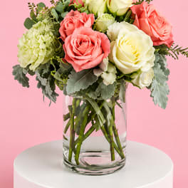 Pink and white roses in a clear glass vase with green filler flowers