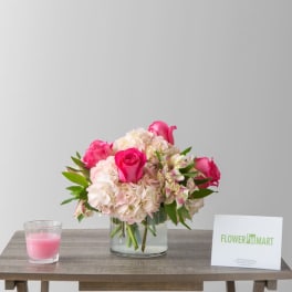 Pink and white flower arrangement in a glass vase with a pink candle beside it