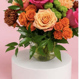 Bouquet of pink and peach roses with orange blooms in a glass vase