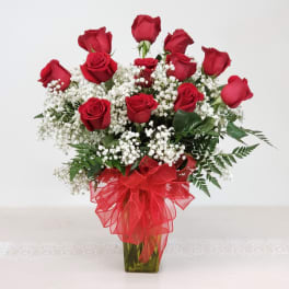 Red roses arranged in a glass vase with white baby's breath and a red ribbon