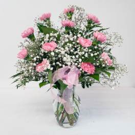 Pink carnations in a glass vase with baby's breath and a pink ribbon