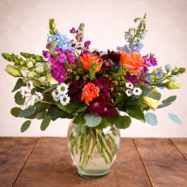 Mixed bouquet of orange, purple, and blue flowers in a clear glass vase