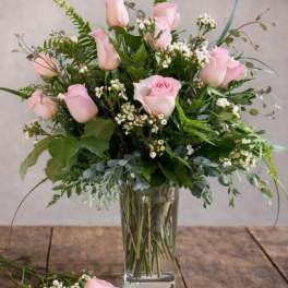 Pink roses arranged in a clear glass vase with mixed greenery.