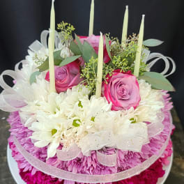 Round floral arrangement with pink roses, white daisies, and tall candles
