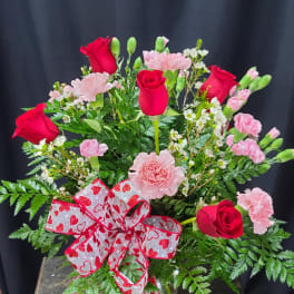 Bouquet of red roses and pink carnations in a glass vase with a heart ribbon