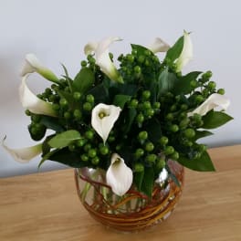 White calla lilies in a glass vase with green berry clusters