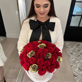 Round box of red and gold roses held in front of a woman in a dress