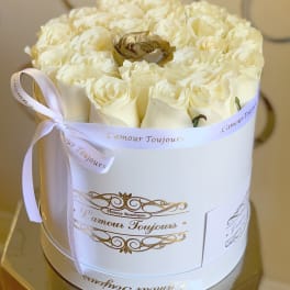 Round white box filled with cream roses and a single gold rose, tied with a white ribbon.