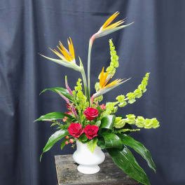 Tall tropical arrangement with red roses and bird of paradise in a white vase