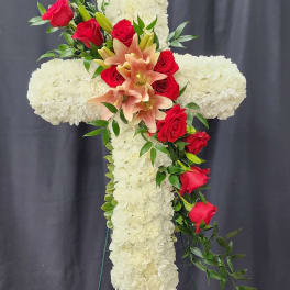 White floral cross with red roses and peach lilies on a stand