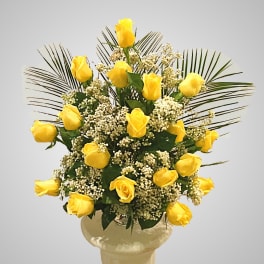 Yellow roses arranged in a vase with white filler flowers and palm fronds