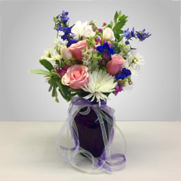 Bouquet of pink roses, white daisies, and blue flowers in a purple vase