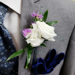 White and purple boutonniere with green leaves on a gray suit lapel