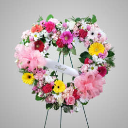 Heart-shaped floral wreath with pink, white, and yellow flowers and a ribbon