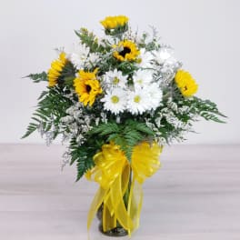 Bouquet of white daisies and yellow sunflowers in a glass vase with a yellow ribbon