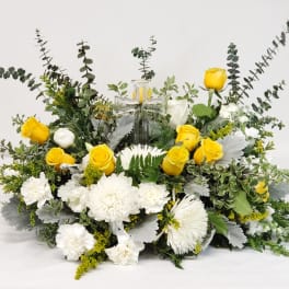 Yellow roses and white flowers arranged around a glass cross.