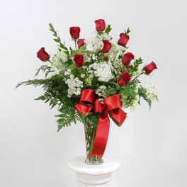 Red roses and white filler flowers in a clear glass vase with a red ribbon