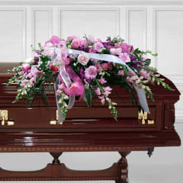 Pink floral spray on a casket with white ribbons