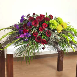 Long floral centerpiece with red, purple, and yellow blooms on a white table