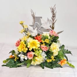 Floral arrangement with yellow, pink, and white blooms around a dove cross