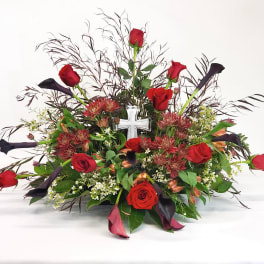 Red roses and dark calla lilies in a low floral arrangement with a white cross