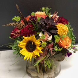 Mixed bouquet in a glass vase with a sunflower, roses, and bright accent flowers