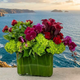 Arrangement of green hydrangeas, orchids, roses, and calla lilies in a glass vase