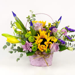 Mixed bouquet in a pink basket with yellow, purple, and lavender flowers