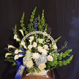 White floral arrangement with calla lilies, roses, and blue ribbon in a basket