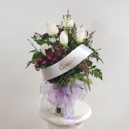 White roses in a glass vase with a lavender ribbon and sash