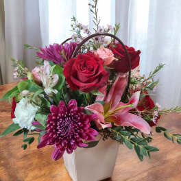 Mixed flower arrangement in a white handled box with red roses and pink lilies