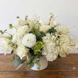 White floral arrangement in a white vase with roses, hydrangeas, and calla lilies