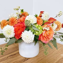 Mixed orange, white, and coral flowers arranged in a white vase