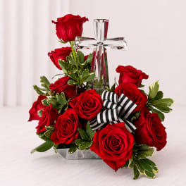 Red roses arranged around a clear glass cross with a striped ribbon