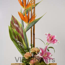 Tropical floral arrangement with orange bird-of-paradise and pink lilies in a green vase