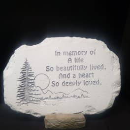 Memorial stone plaque with engraved trees and text on a stand