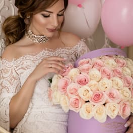 Woman in lace dress holding a lavender hat box filled with pink and cream roses