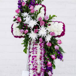 Cross-shaped floral tribute with pink roses, white chrysanthemums, and purple orchids