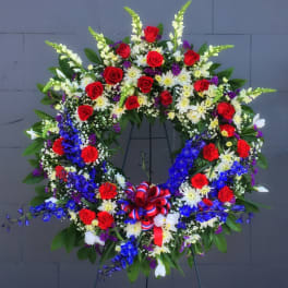 Large circular floral wreath with red roses, white daisies, and blue flowers