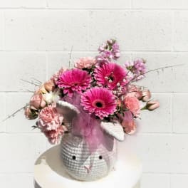 Pink floral arrangement in a textured bunny-shaped container with a tulle bow