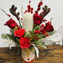 Holiday arrangement with red roses, carnations, and reindeer antlers in a decorative vase