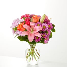 Pink lilies, roses, and purple daisies in a clear glass vase