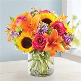 Bouquet of orange lilies, pink roses, and sunflowers in a clear glass vase