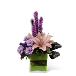 Pink lily and purple flowers in a square glass vase